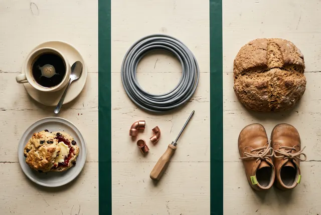 Three groups of items on a table: coffee and a scone, electrical cable and pipe fittings, soda bread and children's shoes